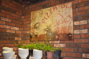 Ein Wandbild von Pizza-Blitz im Industrial- und Vintage-Look. Darunter frische Kräuter zum selber pflücken.